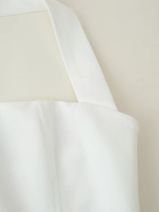 Detail eines weißen Neckholder-Kleides mit feiner Stoffstruktur und breiten Schulterträgern