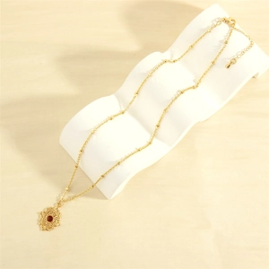 Detail of 18K gold-plated pendant necklace with red gemstone on white wave display