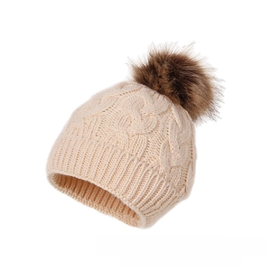 Detailed cable knit pattern on beige winter hat with brown faux fur pompom decoration