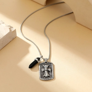 Close-up of vintage silver chain necklace with cross tag and black bullet pendant