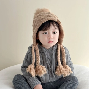Detail of beige knit winter hat with large pom-pom and thick braided tassels on grey hoodie