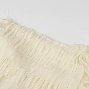 Detailed close-up of layered fringe tassels on cream mesh long sleeve blouse fabric
