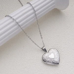 Close-up of heart-shaped stainless steel locket necklace with floral engraving on roman pillar