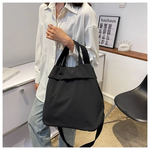 Minimalist black nylon tote bag worn by a model in a modern white studio setting