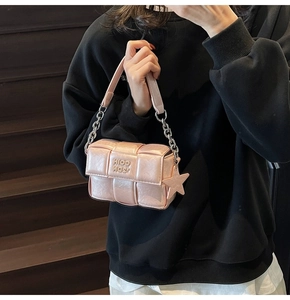 Détail du sac à bandoulière tressé rose avec chaîne argentée et breloque étoile sur l'escalier