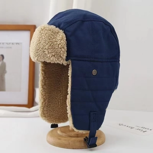 Detail of blue pilot winter hat with beige sherpa lining and earflaps on wooden stand