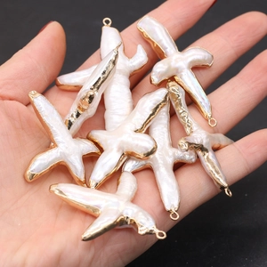 Main tenant des pendentifs croix en perles baroques d'eau douce avec bords dorés et anneaux