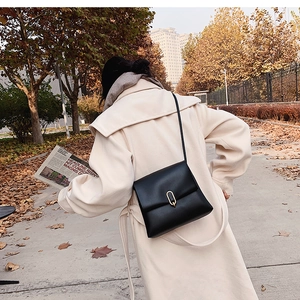 Détail du sac à bandoulière en cuir noir avec boucle dorée dans une scène de rue d'automne