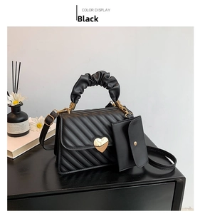 Detail of black quilted shoulder bag featuring gold heart clasp and ruffled handle