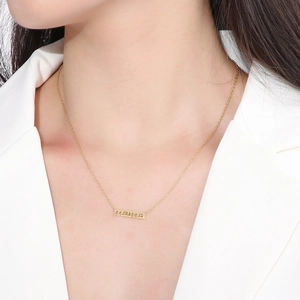Macro shot of gold stainless steel mama pendant necklace worn by a model in a white suit