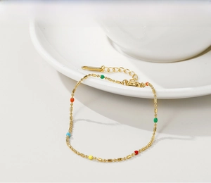 Detailaufnahme einer goldfarbenen Edelstahlkette mit bunten Emaille-Perlen auf weißem Porzellan