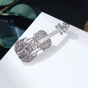 Dettaglio ravvicinato di una spilla a violino argento con strass pavé su marmo bianco