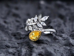 Macro detail of leaf-shaped silver ring with pear-cut yellow gemstone on dark rock
