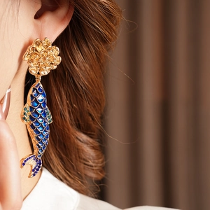 Detail of vintage gold fish earrings with blue enamel scales and floral stud on model