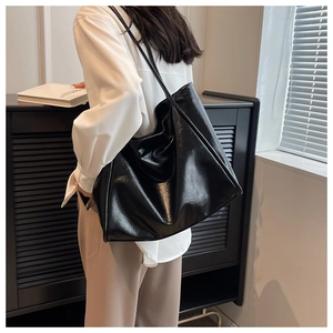 Détail d'un grand sac cabas noir en cuir huilé brillant porté par un mannequin