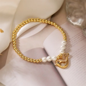 Dettaglio del bracciale elastico con perline dorate, perle e ciondolo a forma di uccello
