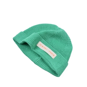 Detail der Strickstruktur einer hellgrünen Beanie mit weißem rechteckigem Aufnäher