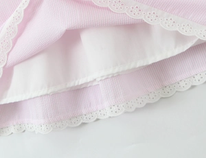 Close-up of pink and white striped fabric with intricate white lace embroidery hem