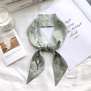 Detailed flat-lay of sage green silk scarf featuring floral prints and letter Y design
