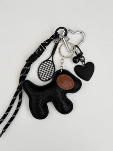 Detail of dog charm and tennis racket keychain with silver heart-shaped carabiner