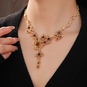 Close-up of a vintage flower necklace featuring deep red and amber gemstones on a model