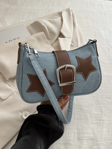 Detail of blue denim shoulder bag featuring brown leather stars and metallic buckle closure