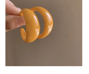 Detailed close-up of glossy orange C-shaped acrylic earrings held in hand