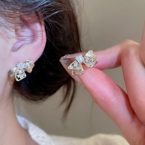 Detailed view of silver needle bow earrings with cubic zirconia worn on female model ear