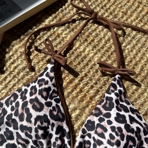 Detail of leopard print bikini top with brown halter ties on a woven straw background