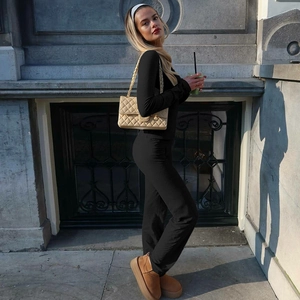 Side view of woman in black slim fit long sleeve top and flared trousers on street