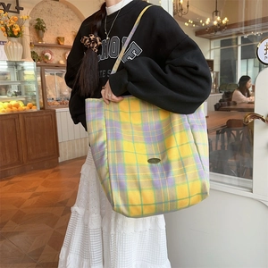 Close-up of a large checkered canvas tote bag with a metallic logo plate in a cafe setting