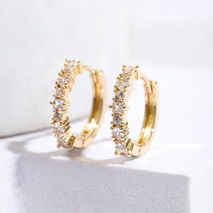Close-up of gold hoop earrings with square blue zircon inlay on white minimalist background