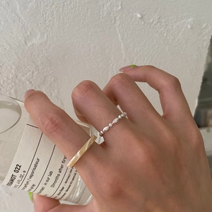Silver bead chain and cream marble resin rings worn by a model holding a perfume bottle