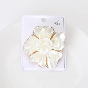 Close-up of elegant white floral brooch with gold edges and crystals on jewelry card