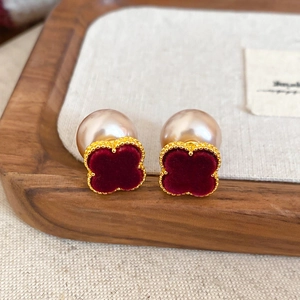 Detailed macro of a red flocked clover earring with golden beads and a champagne pearl