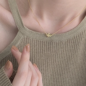 Close-up of minimalist bird pendant on a thin gold chain worn on the collarbone