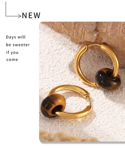 Macro shot of gold titanium hoop earring with natural tiger eye stone bead on white sand
