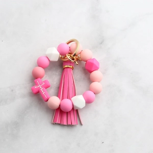 Dettaglio del bracciale in silicone rosa con ciondolo a croce Jesus e nappa in pelle