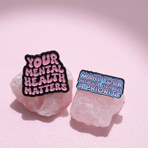 Enamel pins featuring Your Mental Health Matters and Priority slogans on pink stone