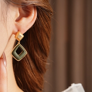 Close-up of geometric gold and dark green rhombus earrings worn by a model