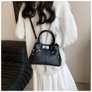 Detail of black pebbled leather handbag with silver turn-lock and adjustable strap