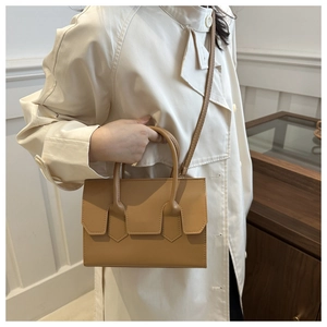 Detail of tan leather handbag with top handle and strap held against a beige trench coat