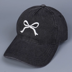 Detailaufnahme der weißen Schleifenstickerei auf der schwarzen Denim-Baseballkappe