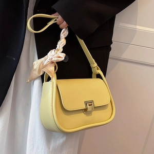 Detail of yellow shoulder bag with silk scarf accessory and metal buckle closure