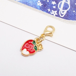 Detail shot of a red enamel strawberry pendant with a gold clasp on a white background