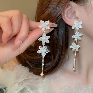 Close-up of white flower earrings with pearls and long tassels on a model