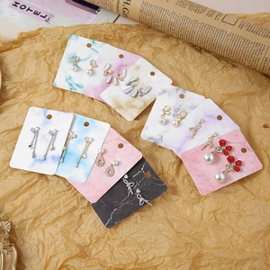Flat lay of multiple pearl and crystal earrings on marble texture display cards