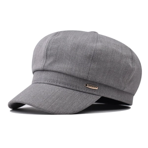 Detail shot of a grey octagonal baker boy hat featuring a rose gold metal logo plate