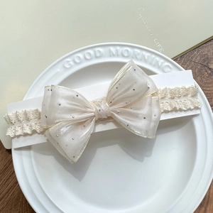Infant lace headband with cream bow featuring silver foil polka dots on a white plate