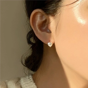 Close-up of model wearing gold heart earrings with clear zircon stones on ears